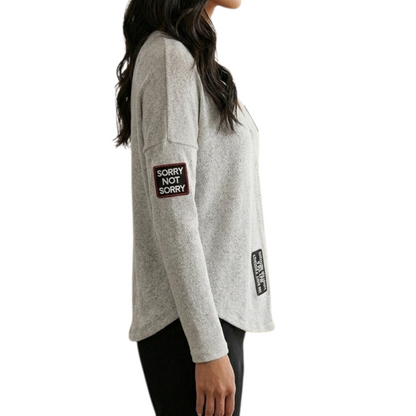 Gray long-sleeve shirt with 'SORRY NOT SORRY' patch on sleeve, worn by a women.