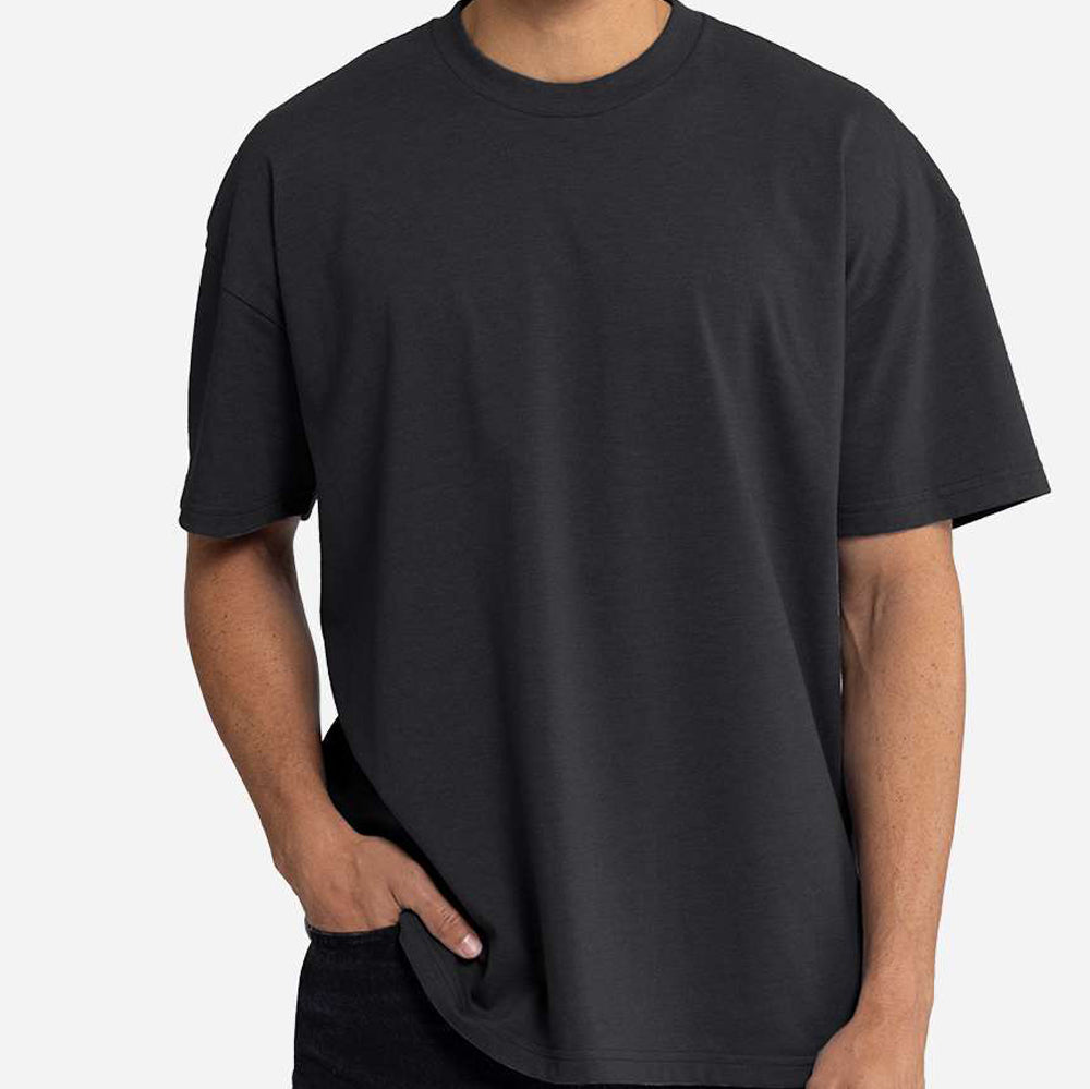 A man wearing a plain black short-sleeve crewneck t-shirt, shown from the neck down against a light gray background. Custom over size shirt print Next Level 7200